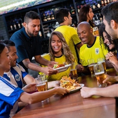 Waiter serving food to a group of friends watching a game at a sports bar - lifestyle concepts
